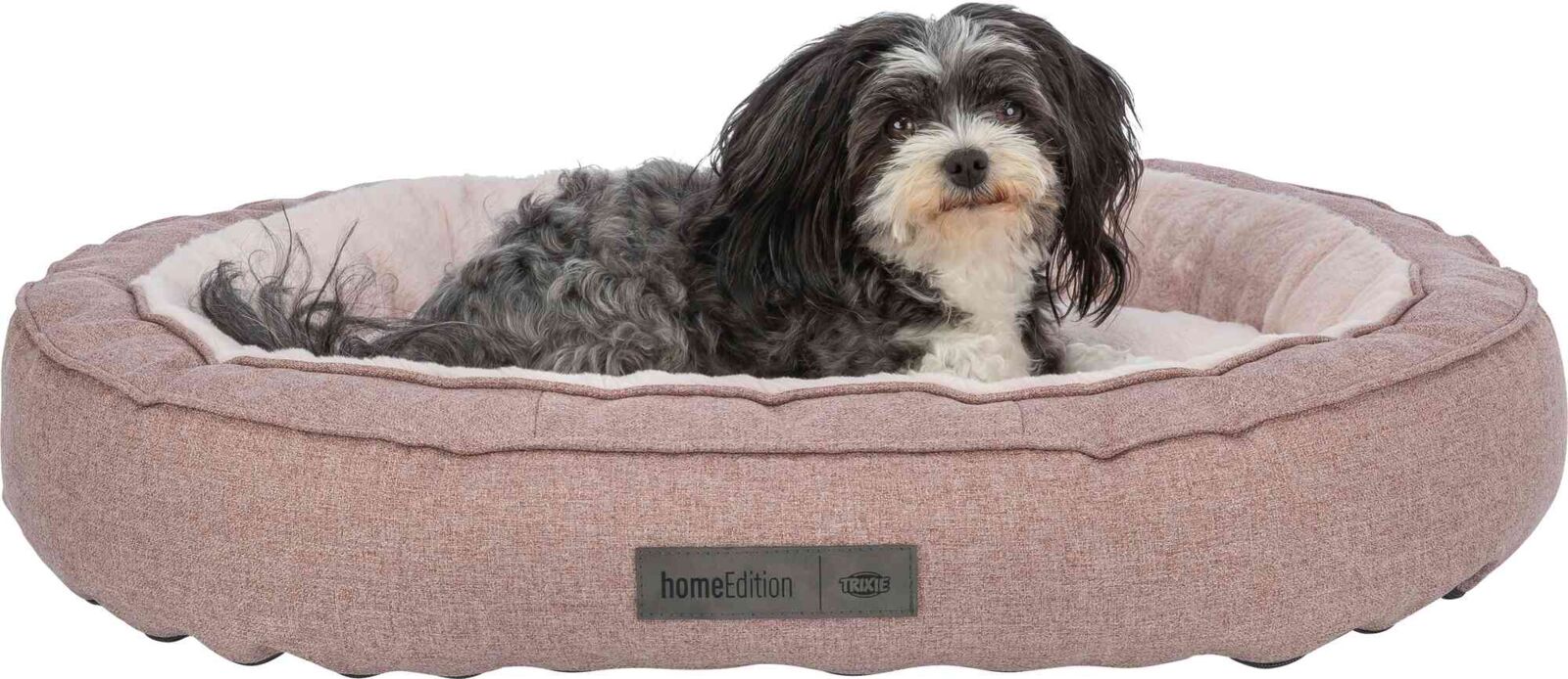 Ein kleiner, schwarz-weißer Hund liegt in einem rosafarbenen, runden Hundebett mit dem Aufdruck "homeEdition".