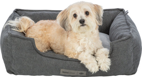 Ein kleiner, beiger Hund liegt in einem grauen, gepolsterten Hundebett mit dem Label "homeEdition".