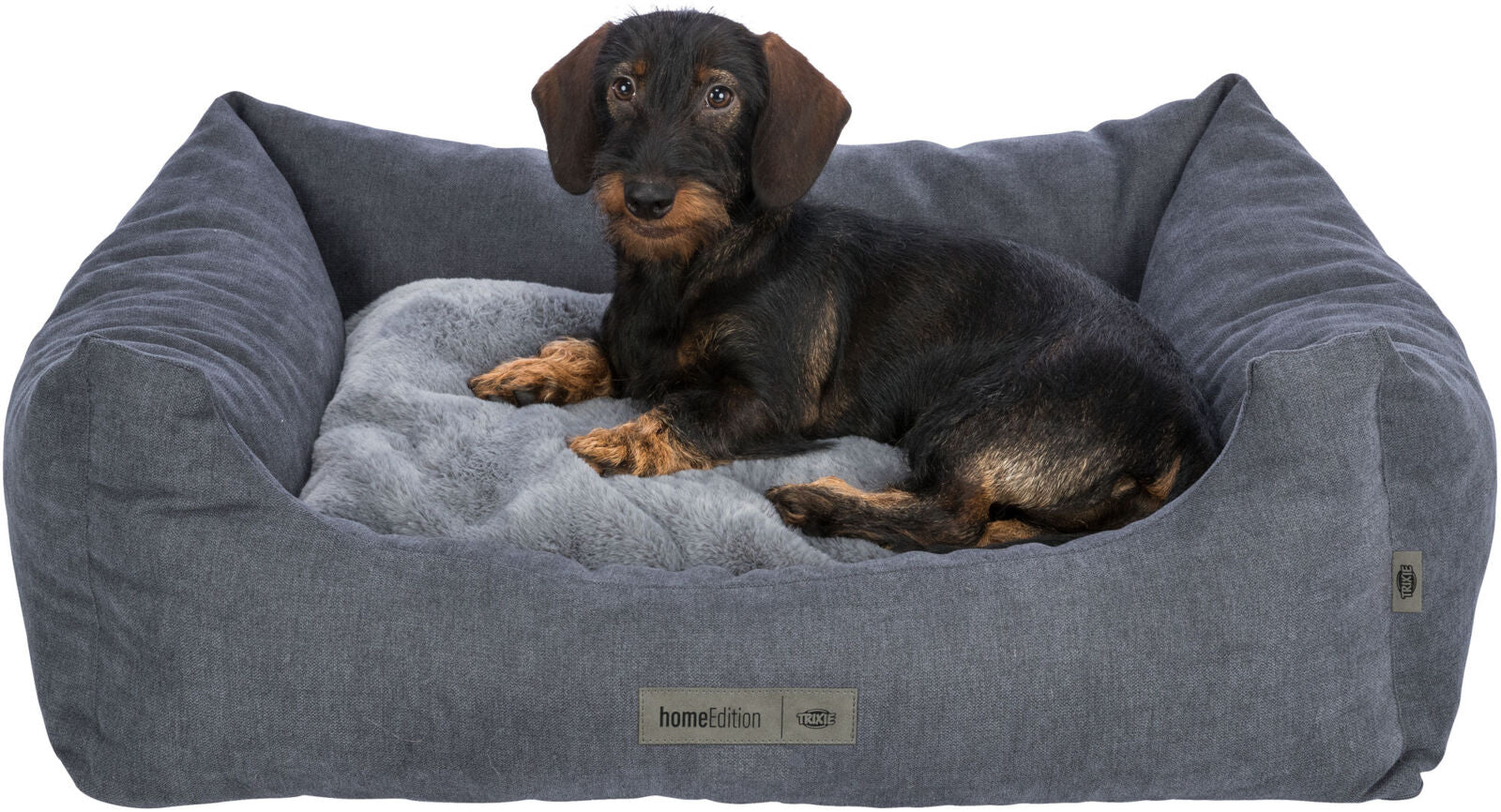Ein Hund liegt in einem grauen Hunde-Sofa mit weichem Kissen, auf dem "homeEdition" steht.