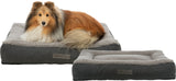 Ein Hund mit langem Fell liegt auf einem grauen, weichen Hundebett mit sichtbarem Logo "vitalEdition Trixie".