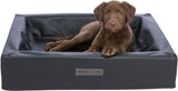 Ein brauner Welpe liegt entspannt in einem dunkelgrauen Hundebett mit einer "homeVITAL" und "TRIXIE" Marke vorn.