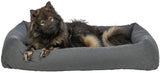 Ein großer, flauschiger Hund liegt in einem grauen Hundebett und schaut nach vorne.