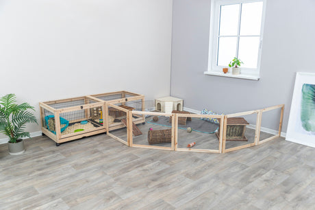 Großes, hölzernes Kleintiergehege mit Gitter in einem Raum mit Holzfußboden, Pflanzen und Fenster.