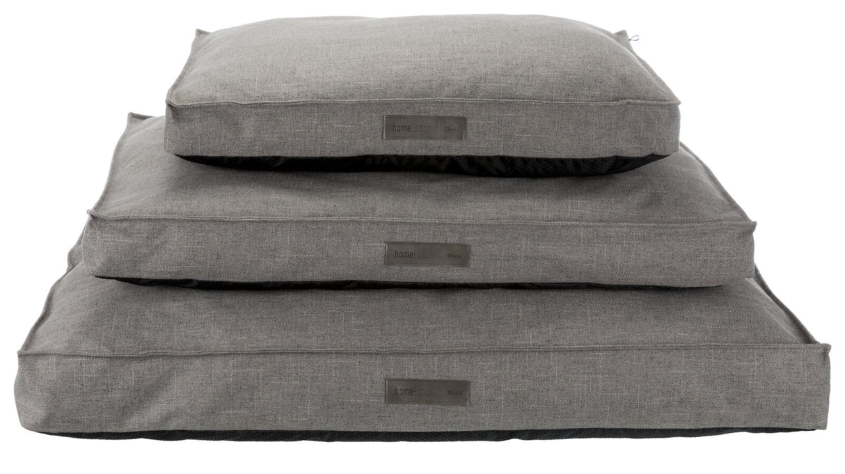 Drei graue Kissen in unterschiedlicher Größe sind gestapelt, jedes mit einem Etikett mit der Aufschrift "homeEdition TRIXIE".