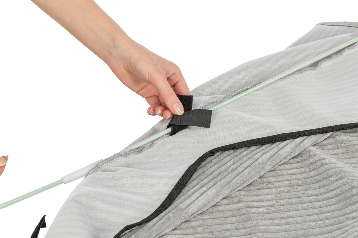 Eine Hand befestigt einen grauen Stab mit schwarzem Klettverschluss an einem gerippten, grauen Stoffbezug.