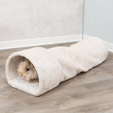 Flauschiger beige Tunnel liegt auf einem Holzboden, ein kleines pelziges Tier schaut heraus.
