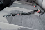 Schwarzer Sicherheitsgurt mit Karabiner auf grauem Autositz, Gurtende an rotem Verschluss befestigt.