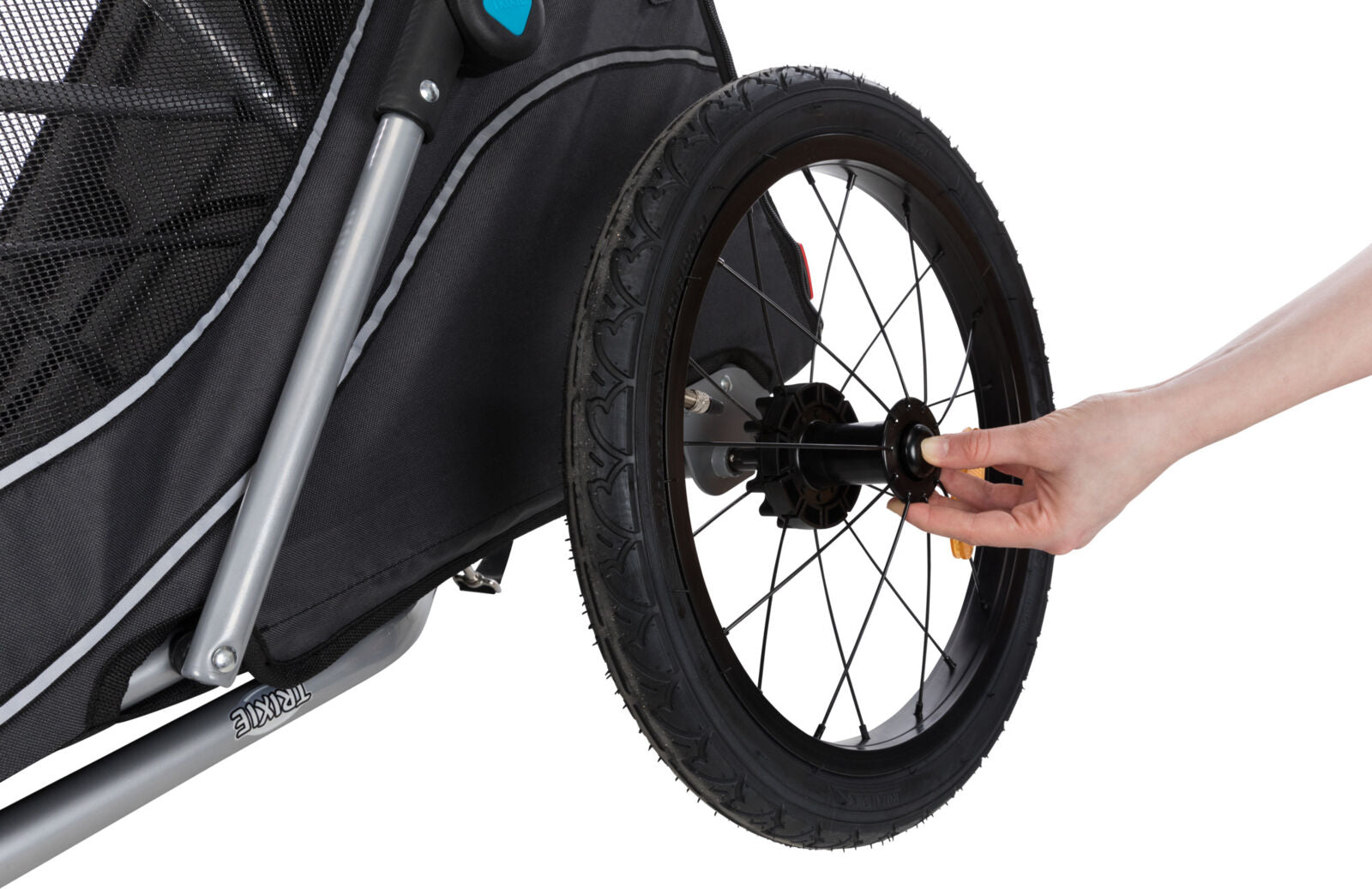Eine Hand befestigt ein Rad an einem schwarzen Fahrradanhänger mit silbernem Rahmen und Netzgewebe.