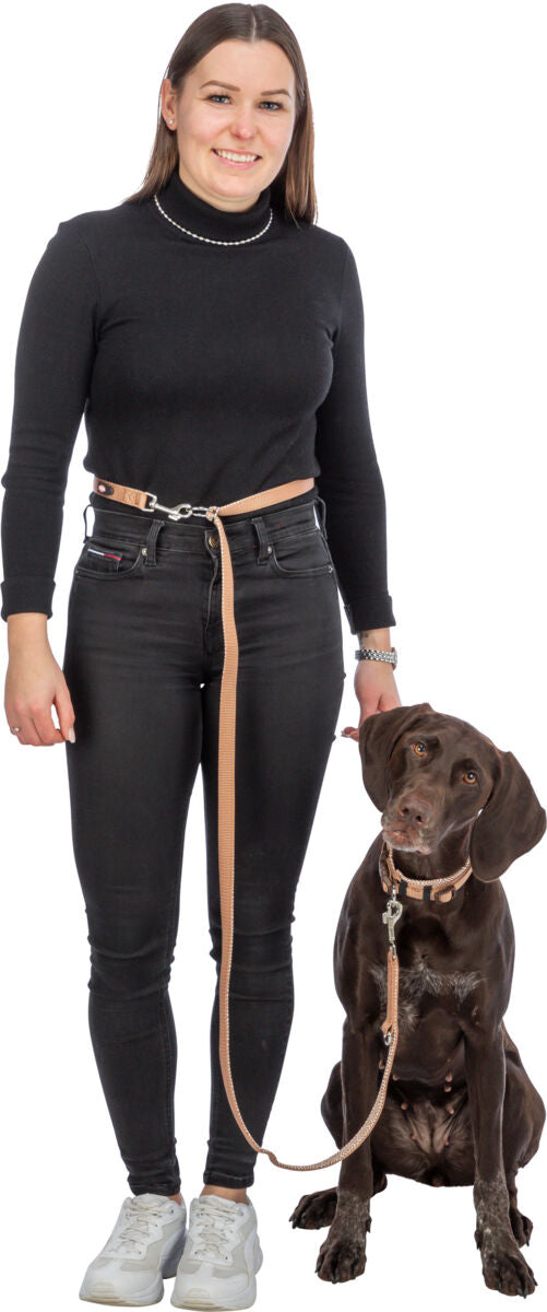 Eine Frau in schwarzem Outfit hält eine Leine, an der ein großer brauner Hund sitzt, auf weißem Hintergrund.