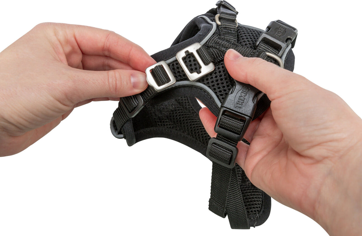 Hände halten schwarzes Hundegeschirr mit Schnallen und verstellbaren Riemen.