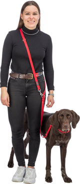 Frau in schwarzem Rollkragenpullover und Jeans hält einen braunen Hund an roter Leine.
