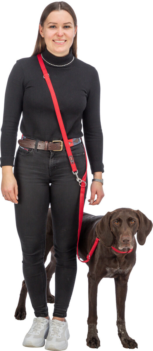 Frau in schwarzem Rollkragenpullover und Jeans hält einen braunen Hund an roter Leine.