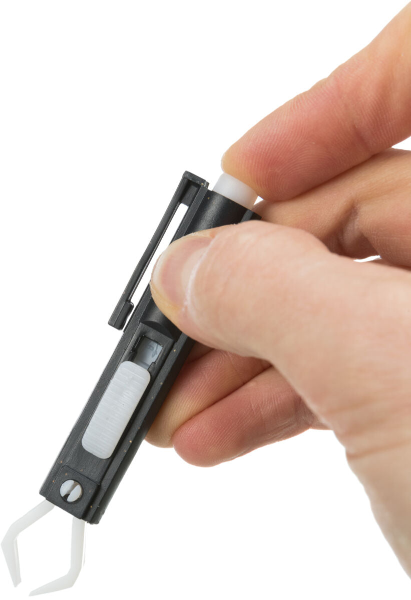 Hand hält ein schwarzes Werkzeug mit weißem Griff und zwei weißen Greifarmen vor weißem Hintergrund.