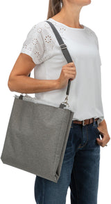 Frau trägt eine graue Stofftasche mit Schulterriemen, weiße Spitzentunika und blaue Jeans.