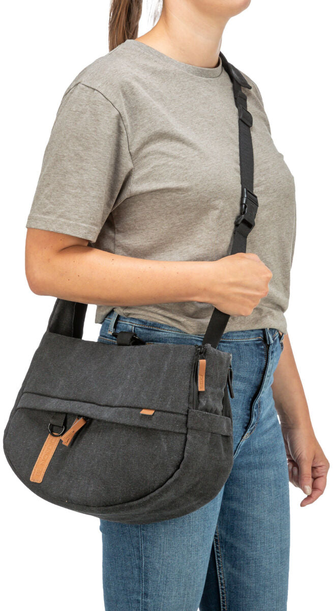 Person trägt eine graue Umhängetasche mit braunen Akzenten, dazu graues T-Shirt und blaue Jeans.