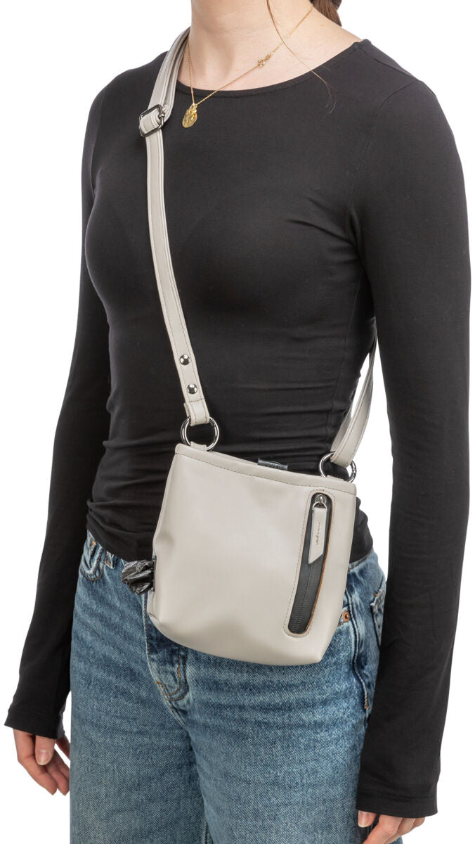 Person mit schwarzem Oberteil trägt eine beige Umhängetasche mit Reißverschluss-Akzent, blauer Jeans.