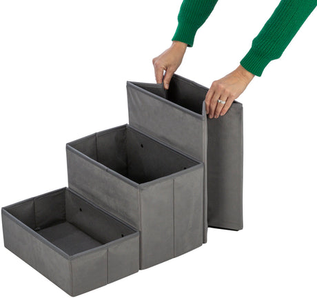 Graue, dreistufige faltbare Aufbewahrungsbox aus Stoff mit einer Person, die die oberste Stufe anhebt.