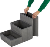Graue, dreistufige faltbare Aufbewahrungsbox aus Stoff mit einer Person, die die oberste Stufe anhebt.