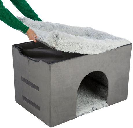 Graue, würfelförmige Höhle mit weichem, abnehmbarem Bezug, Hand hebt obere Abdeckung an.