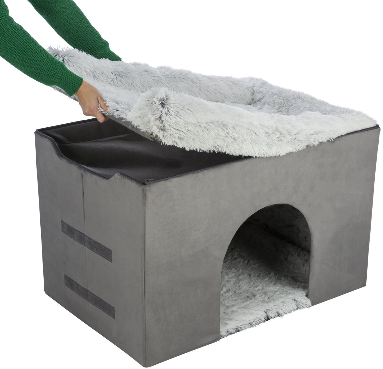 Graue, würfelförmige Höhle mit weichem, abnehmbarem Bezug, Hand hebt obere Abdeckung an.