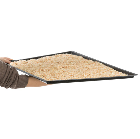 Eine Person hält ein rechteckiges, schwarzes Tablett voller heller, gröberer Partikel vor einem weißen Hintergrund.