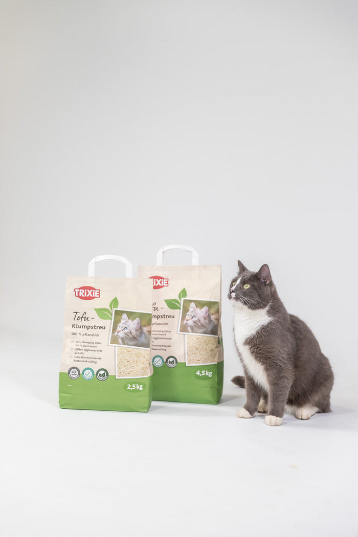 Katze neben TRIXIE Tofu Klumpstreu in 2,5 kg und 4,5 kg Verpackung vor hellem Hintergrund